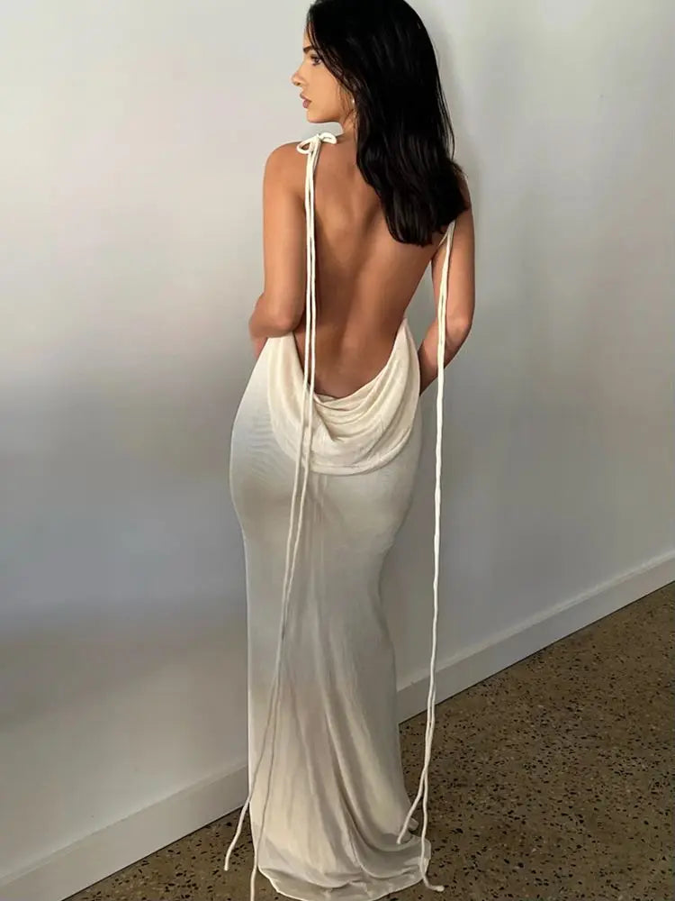 A person wearing a backless, spaghetti strap, maxi dress with a draped silhouette and tie details at the waist.