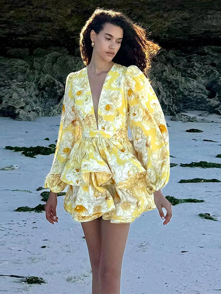 A woman standing by the water wearing a floral print mini dress with long sleeves and a deep v-neck.
