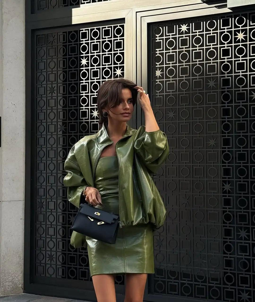 Woman in green outfit holding a black handbag in front of a decorative door.