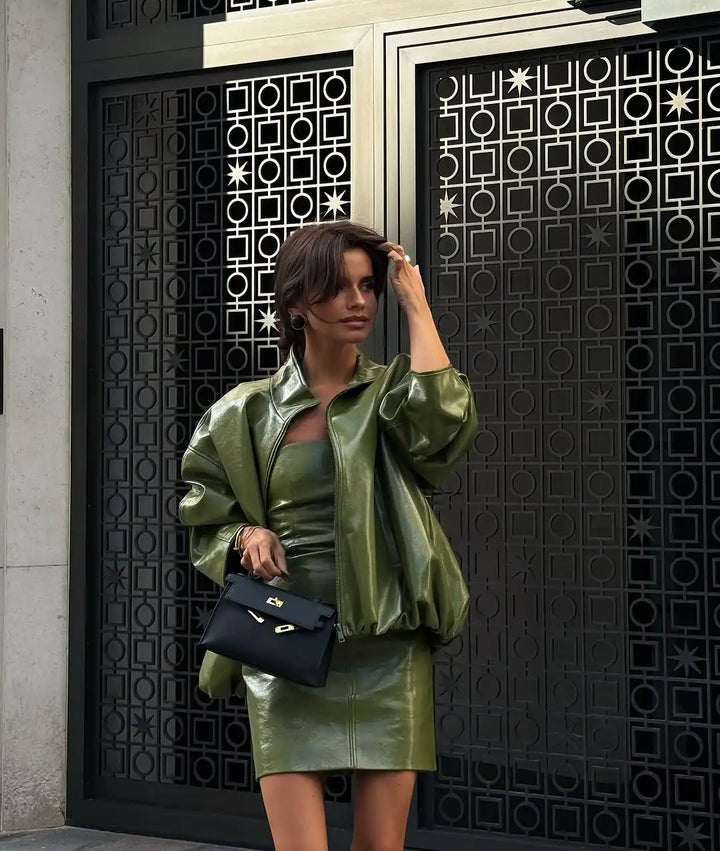 Woman in green outfit holding a black handbag in front of a decorative door.