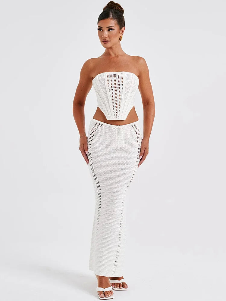 A woman wearing a white two piece set with a strapless bandage crop top and a matching knit skirt.