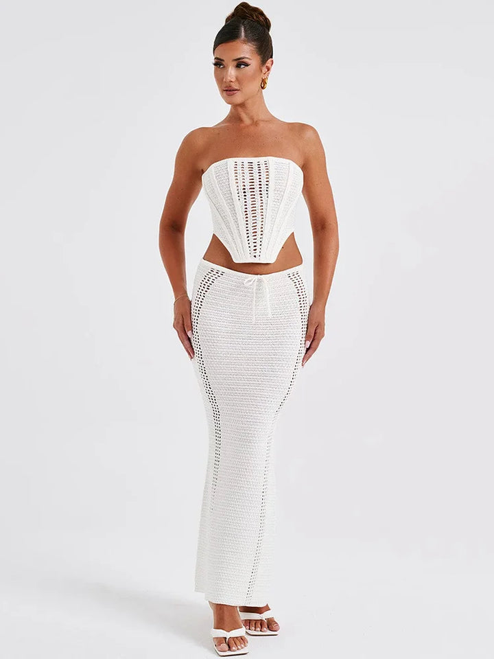 A woman wearing a white two piece set with a strapless bandage crop top and a matching knit skirt.