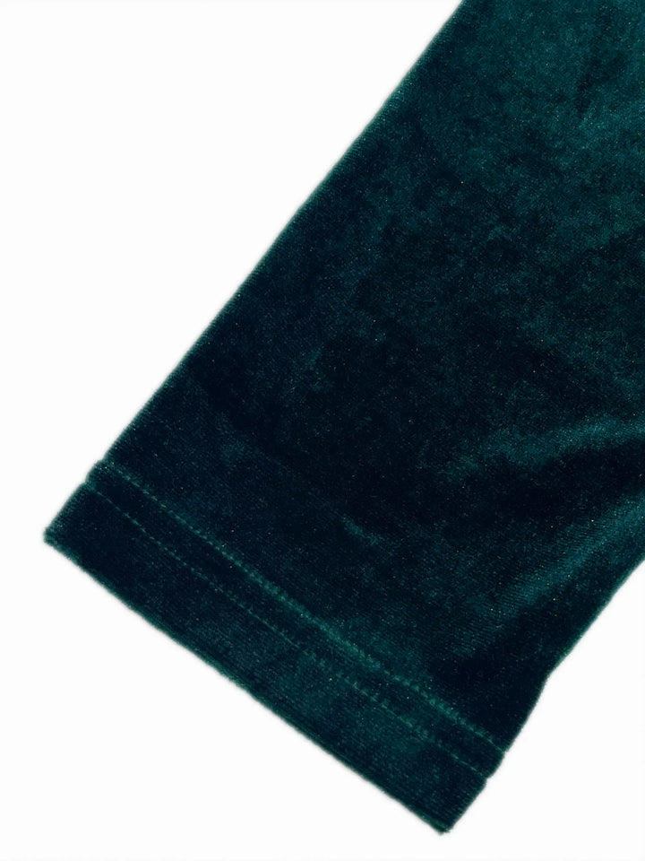 Woman wearing a green velvet one-shoulder dress against a neutral background