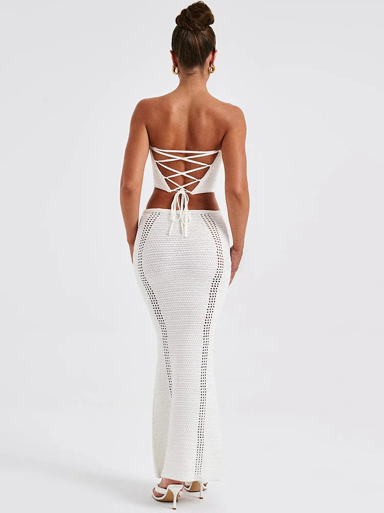 A woman wearing a white two piece set with a strapless bandage crop top and a matching knit skirt.