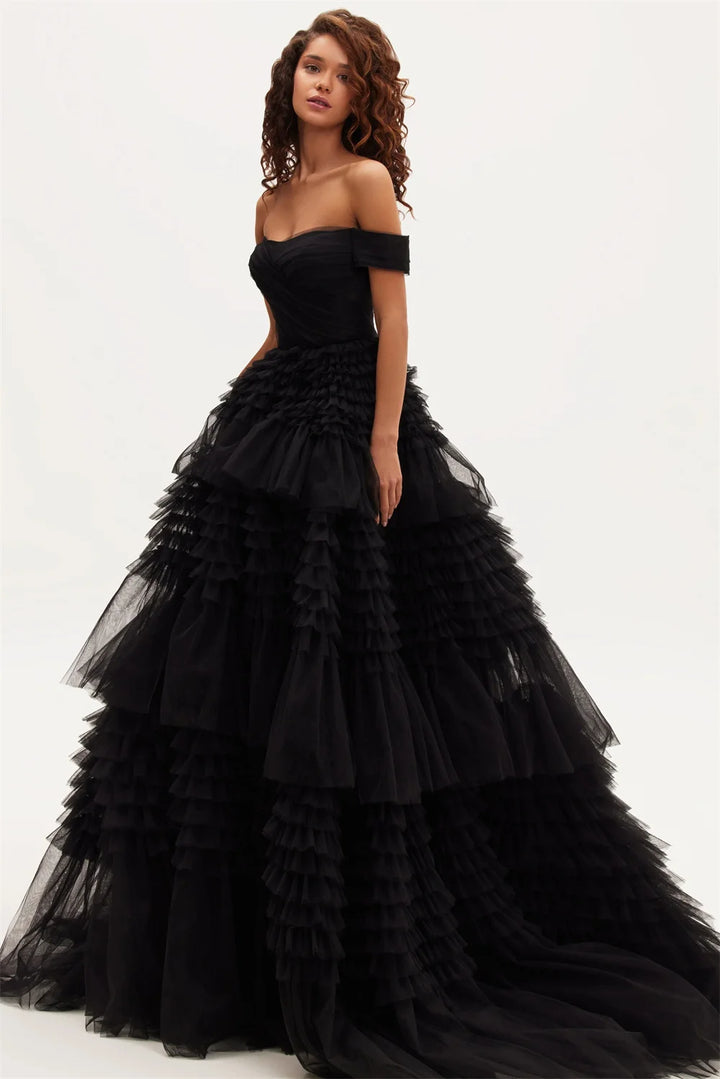 A model wearing an off-the-shoulder black maxi dress with a layered tulle ruffle and organza fabric.