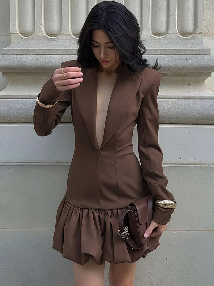 Woman wearing a brown suit with a ruffled skirt against a neutral background