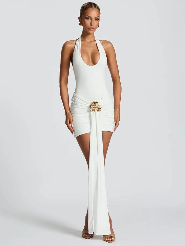 Woman wearing a white halter neck dress with a gold belt on a plain background