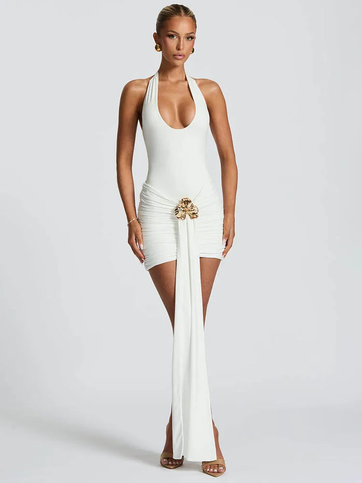 Woman wearing a white halter neck dress with a gold belt on a plain background