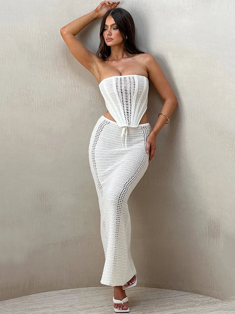 A woman wearing a white two piece set with a strapless bandage crop top and a matching knit skirt.