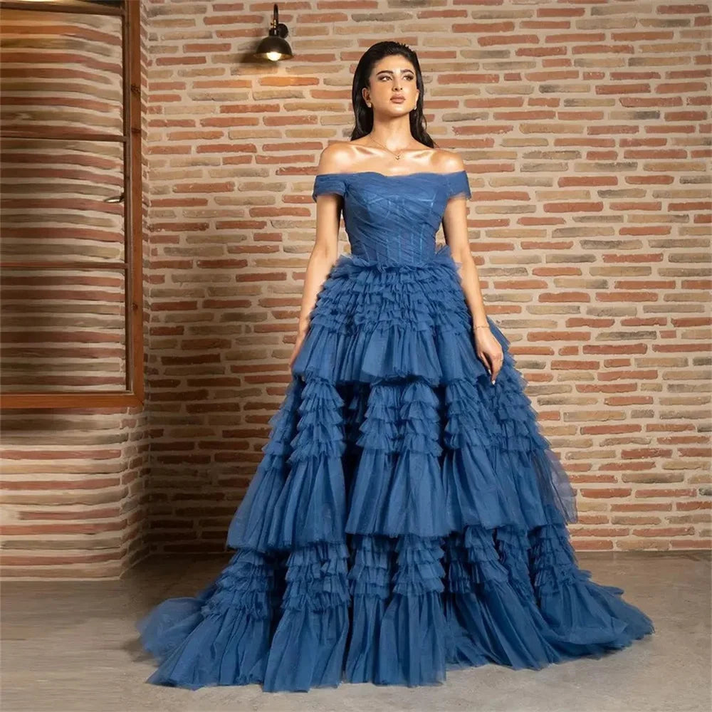 A model wearing an off-the-shoulder blue maxi dress with a layered tulle ruffle and organza fabric.