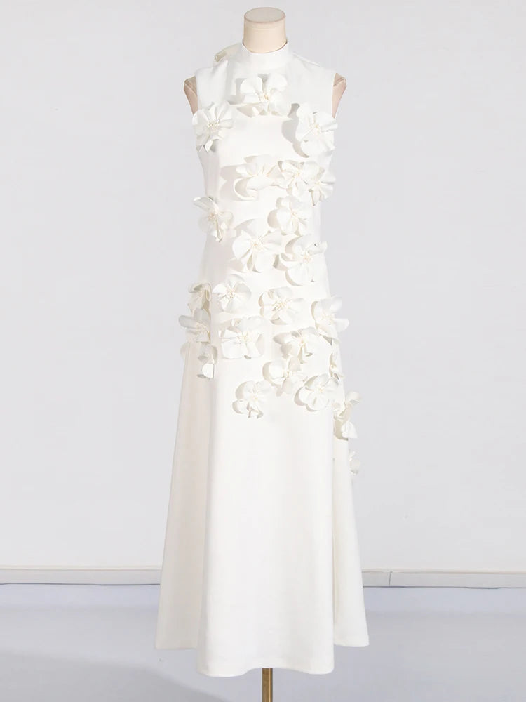 A model wearing a sleeveless, high-waisted, maxi dress with patchwork appliques and a stand collar.