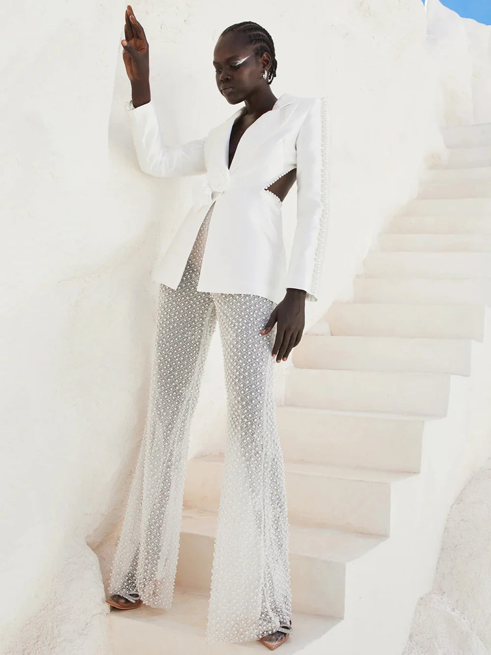 Woman in a stylish white outfit with embellishments standing on a city street.