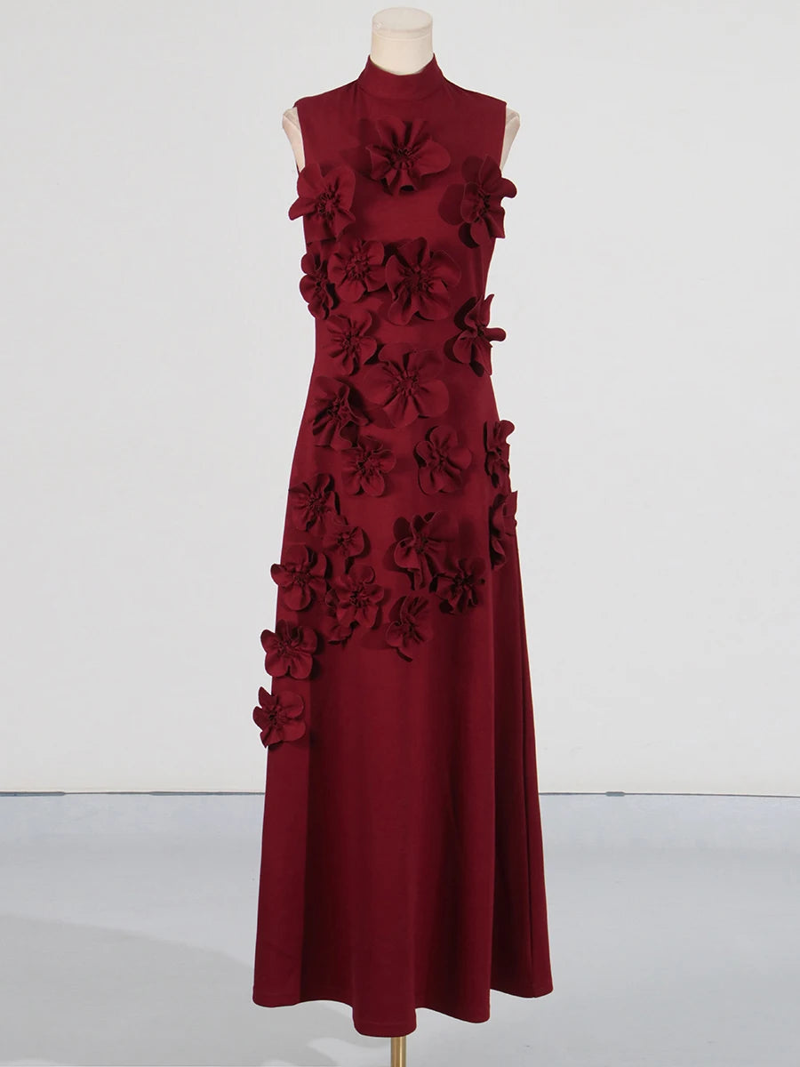 A model wearing a sleeveless, high-waisted, maxi dress with patchwork appliques and a stand collar.