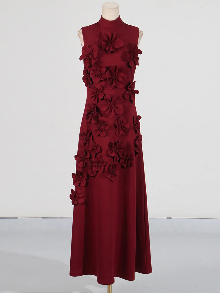 A model wearing a sleeveless, high-waisted, maxi dress with patchwork appliques and a stand collar.