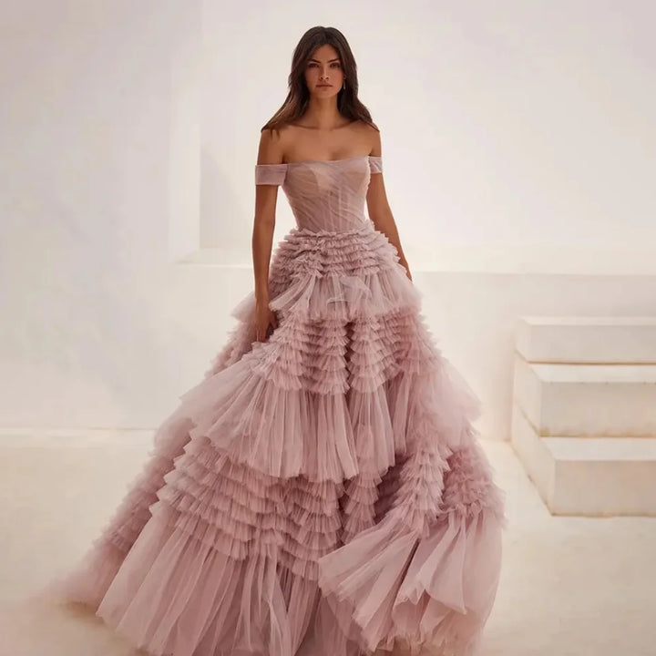 A model wearing an off-the-shoulder pink maxi dress with a layered tulle ruffle and organza fabric.