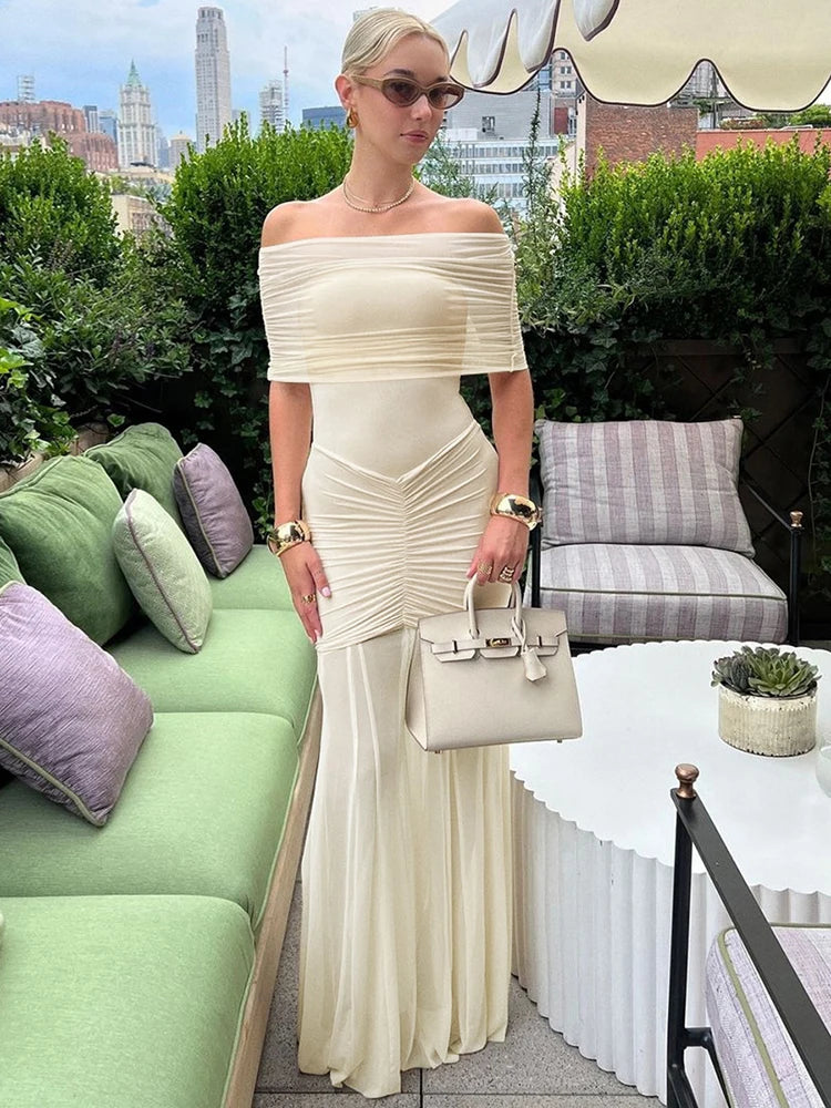 Woman in a white off-shoulder dress holding a handbag on a rooftop with cityscape in the background