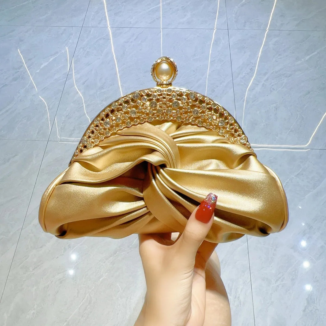 Gold clutch held by a hand against a light gray background