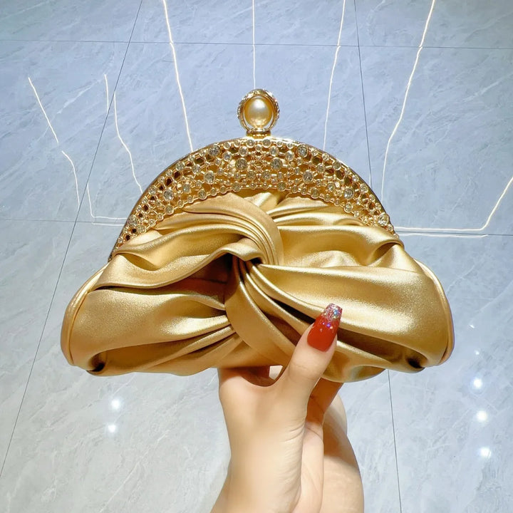 Gold clutch held by a hand against a light gray background