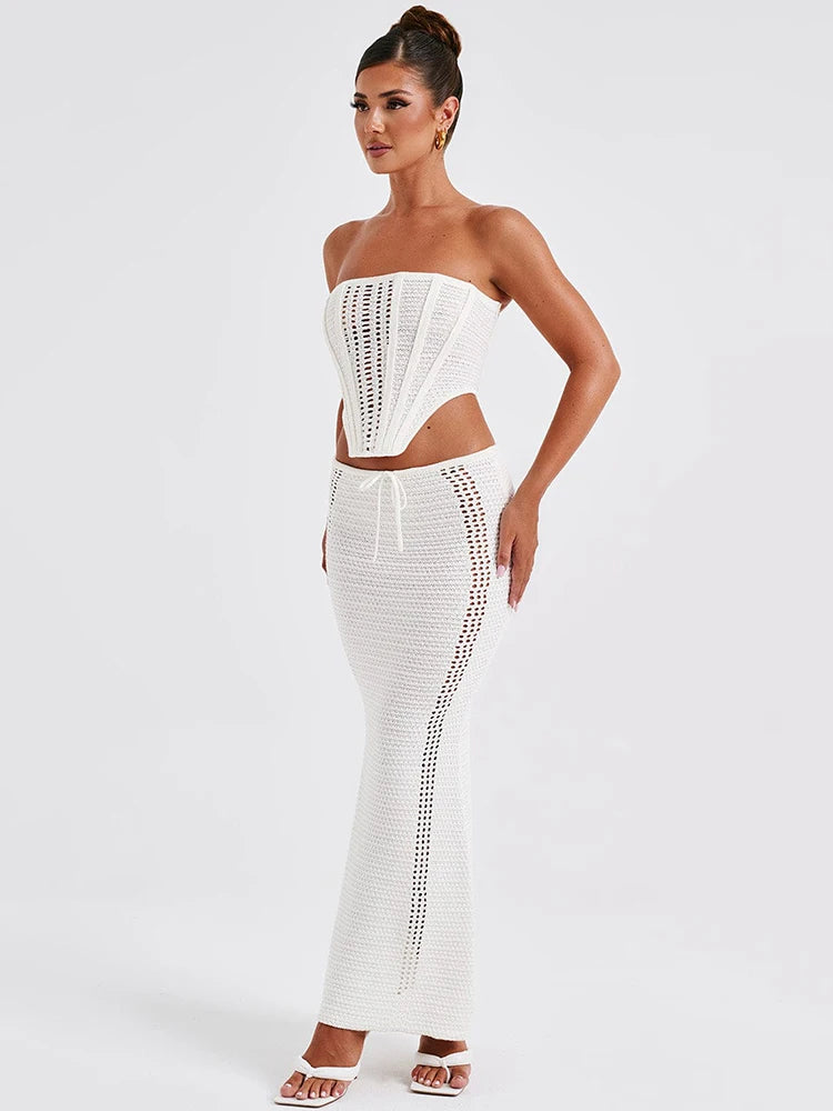 A woman wearing a white two piece set with a strapless bandage crop top and a matching knit skirt.