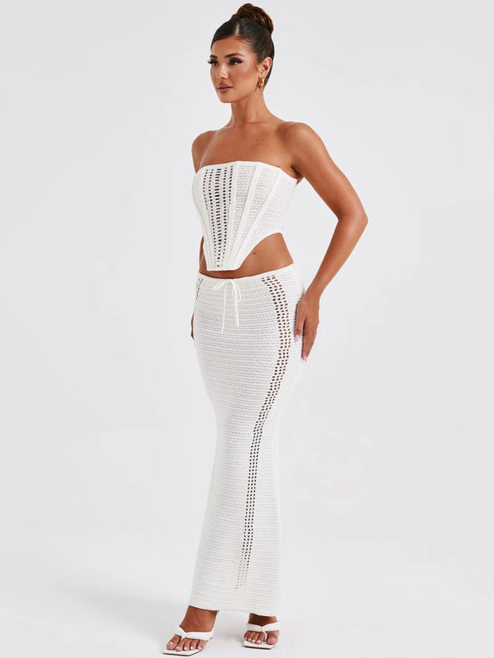 A woman wearing a white two piece set with a strapless bandage crop top and a matching knit skirt.