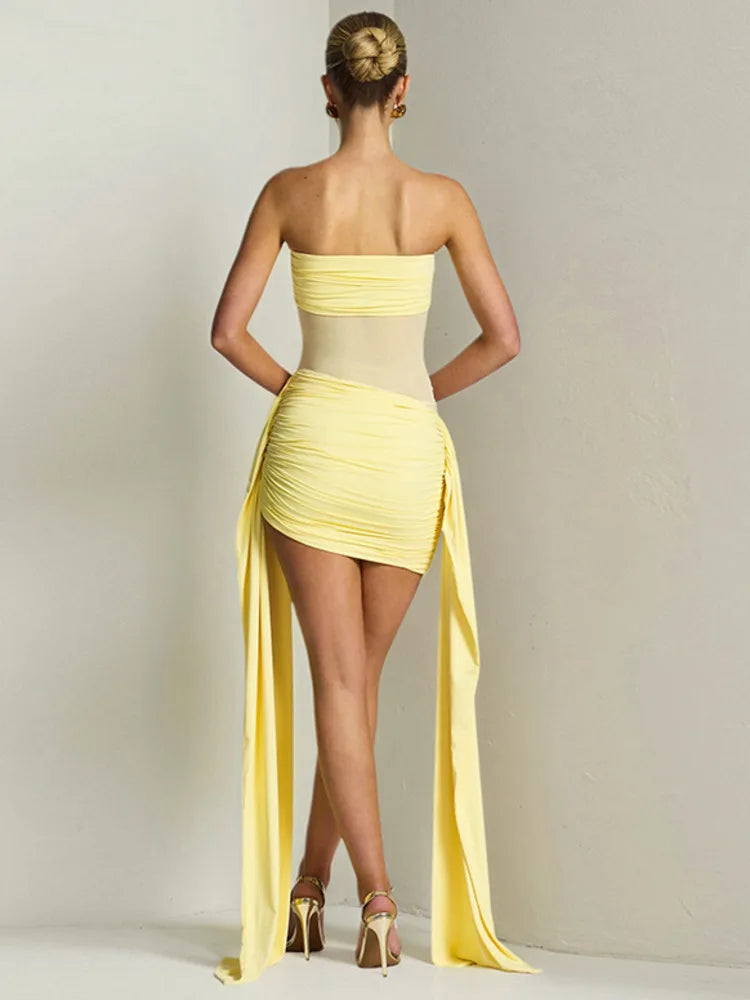 Woman wearing a yellow one-shoulder dress with a long slit on a plain background