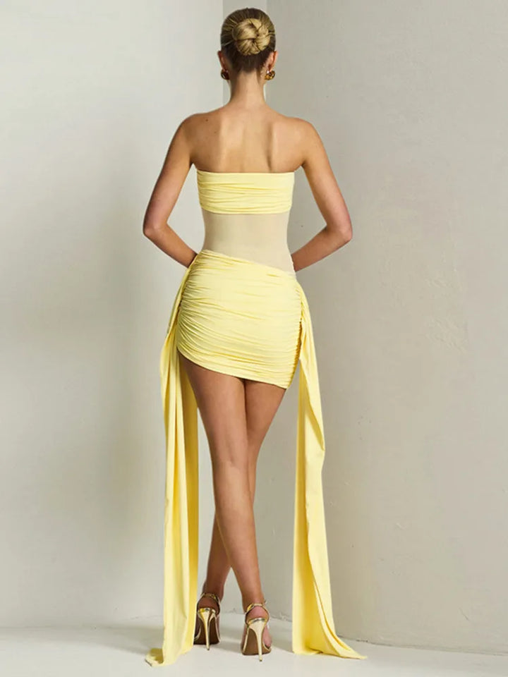 Woman wearing a yellow one-shoulder dress with a long slit on a plain background