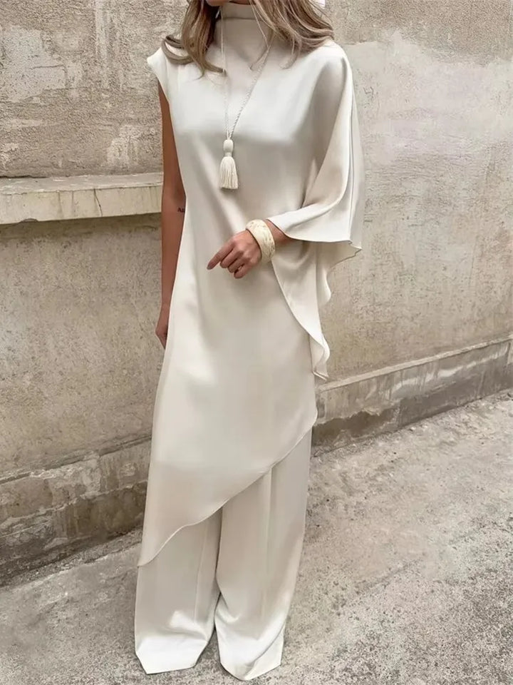 Person wearing a white outfit with a tassel against a textured wall.