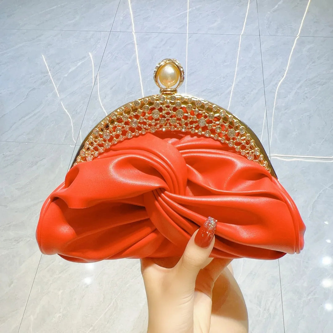 Red clutch with gold detailing held by a hand against a light gray background