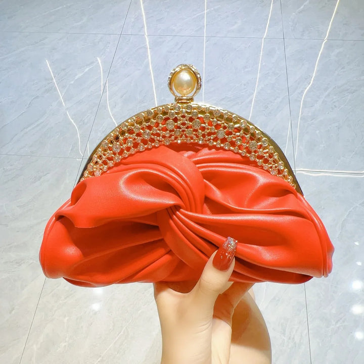 Red clutch with gold detailing held by a hand against a light gray background