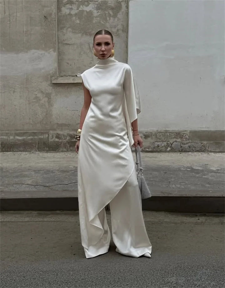 Woman wearing a white dress against a plain wall.