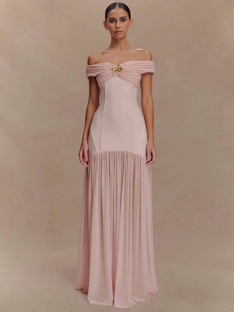 Woman wearing a pink off-shoulder gown with a gold brooch against a beige background