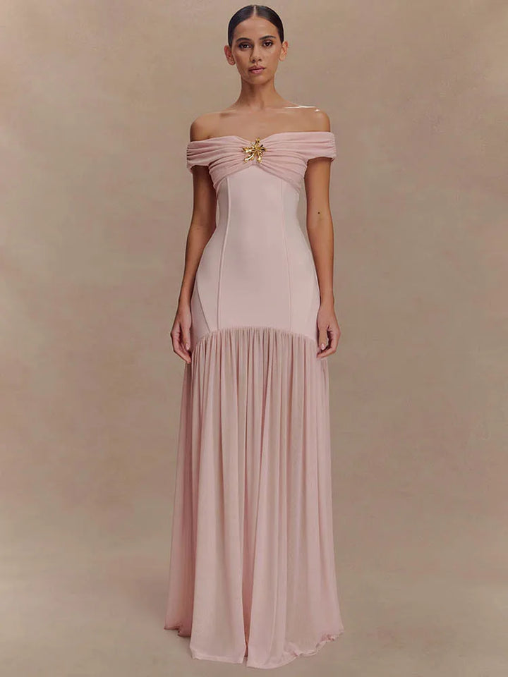 Woman wearing a pink off-shoulder gown with a gold brooch against a beige background