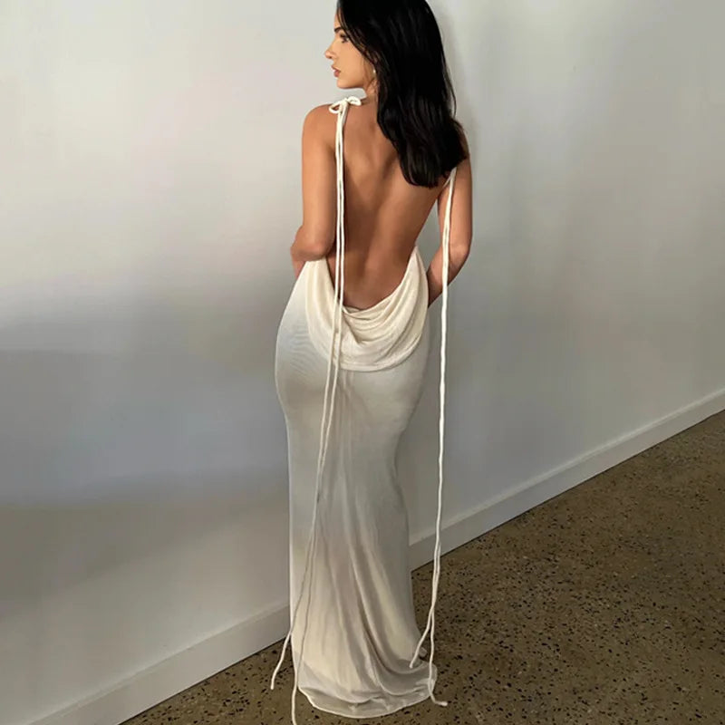 Woman wearing a white dress with a backless design, standing against a plain wall.