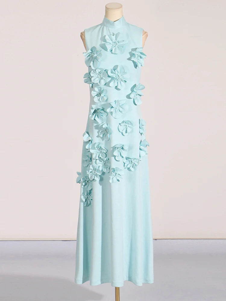 A model wearing a sleeveless, high-waisted, maxi dress with patchwork appliques and a stand collar.