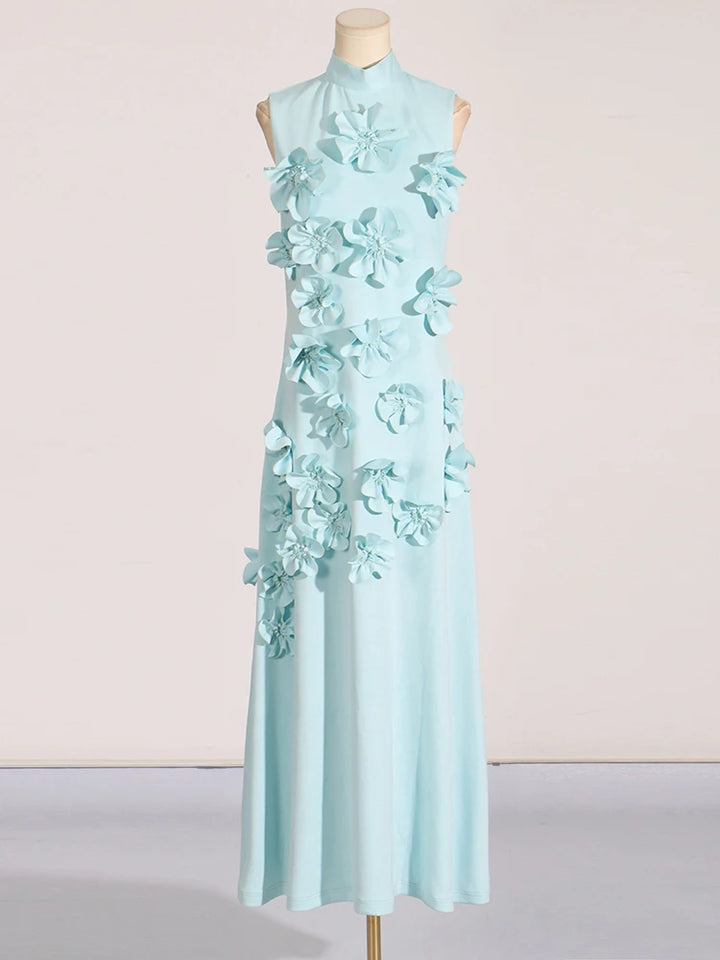 A model wearing a sleeveless, high-waisted, maxi dress with patchwork appliques and a stand collar.