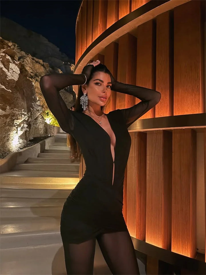 Woman in a black dress posing against a wooden spiral staircase at night.