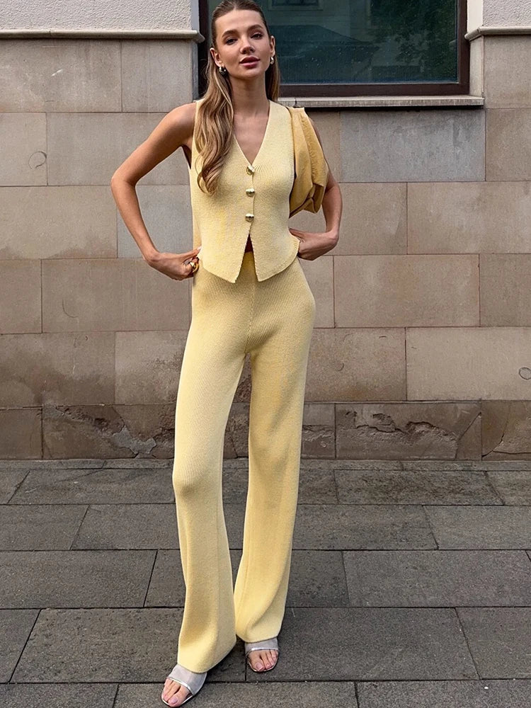 Woman in a yellow outfit standing against a stone wall.