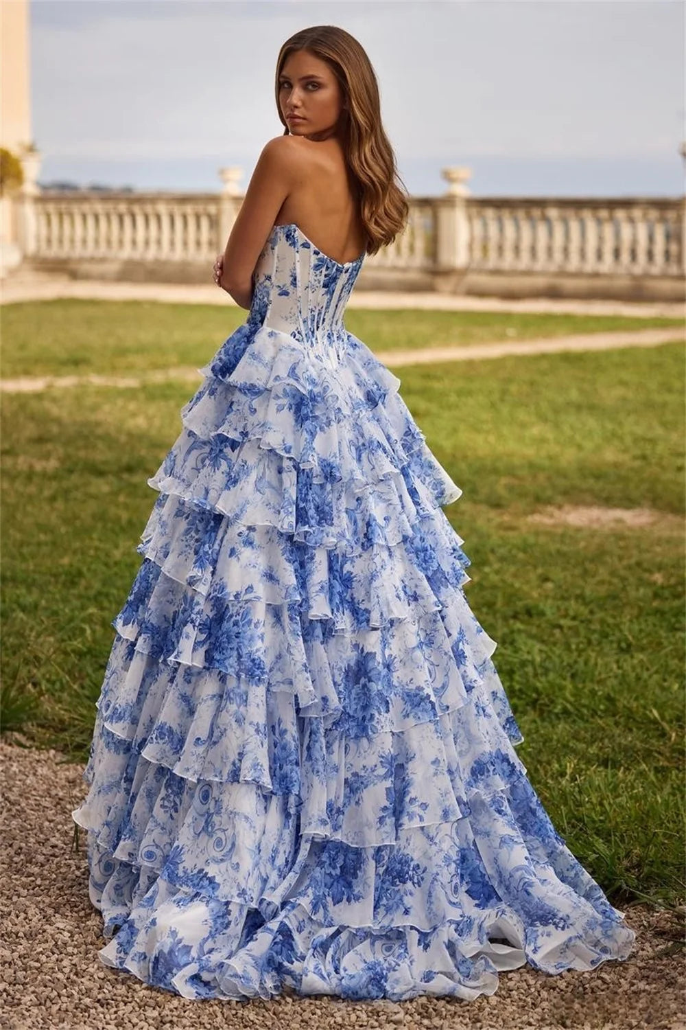 A woman wearing a blue and white floral maxi dress with tiered ruffle detailing and a high side split.