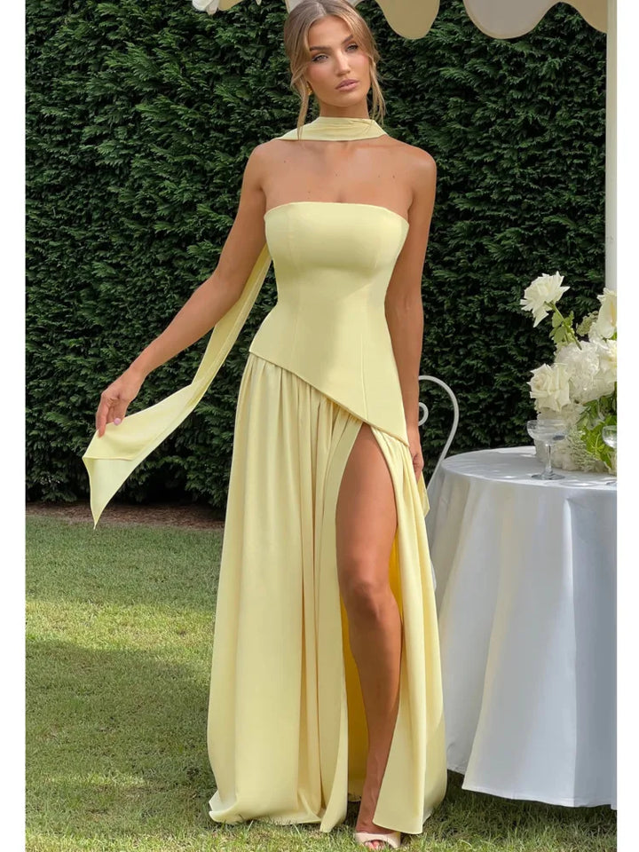 Woman in a yellow dress with a slit standing outdoors near a table with flowers.