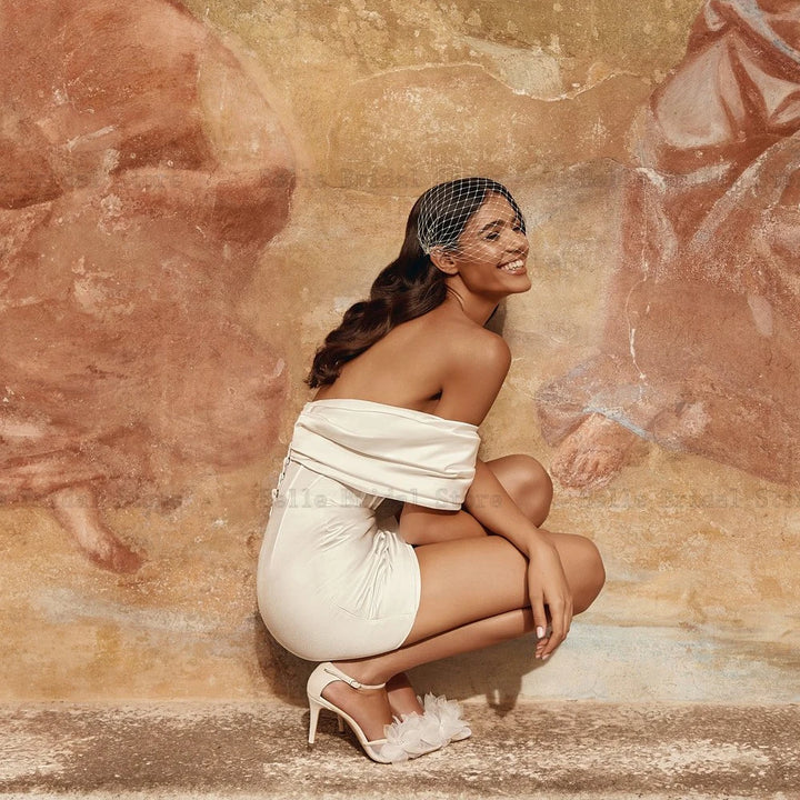 Woman in a white dress crouching against a textured wall with artistic designs.
