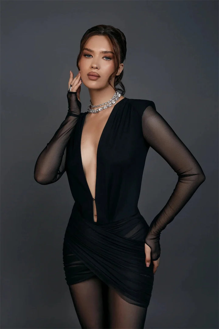 Woman wearing a black dress with sheer sleeves against a dark background