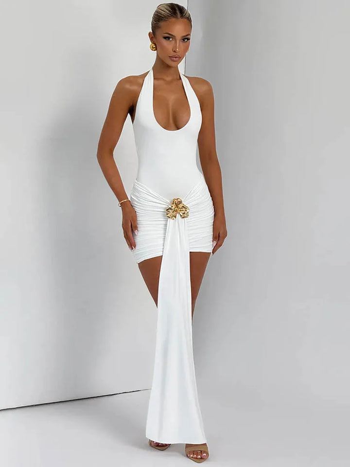 Woman wearing a white halter neck dress with a gold embellishment on a plain background