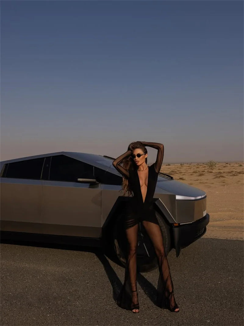Woman in a black dress posing next to a futuristic car in a desert setting