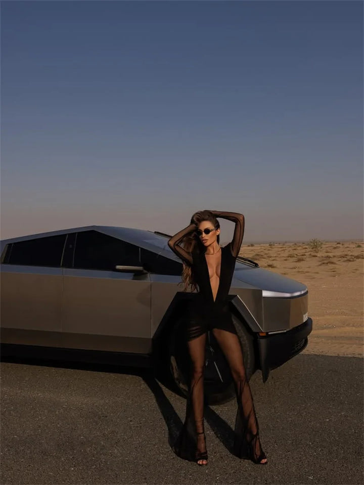 Woman in a black dress posing next to a futuristic car in a desert setting