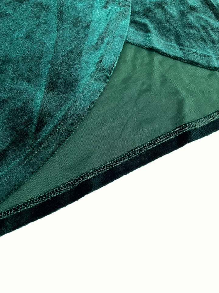 Woman wearing a green velvet one-shoulder dress against a neutral background