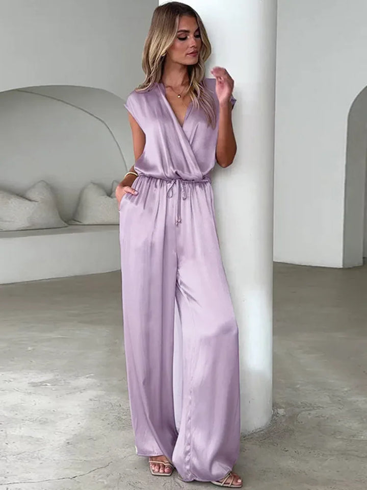 Woman wearing a lavender jumpsuit in a minimalistic room.