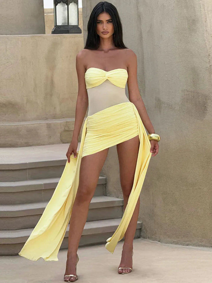 Woman wearing a yellow strapless dress with a high slit, standing outdoors.
