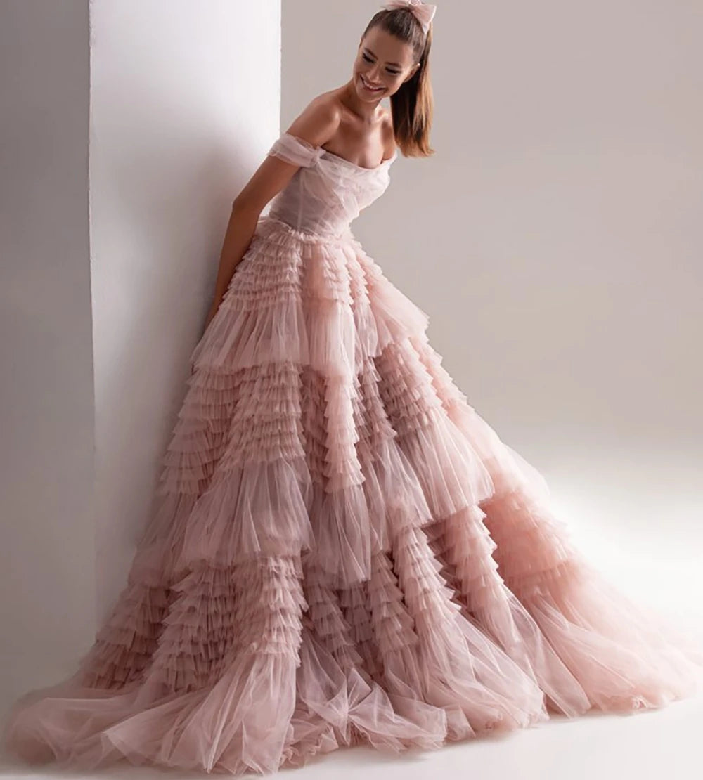 A model wearing an off-the-shoulder pink maxi dress with a layered tulle ruffle and organza fabric.