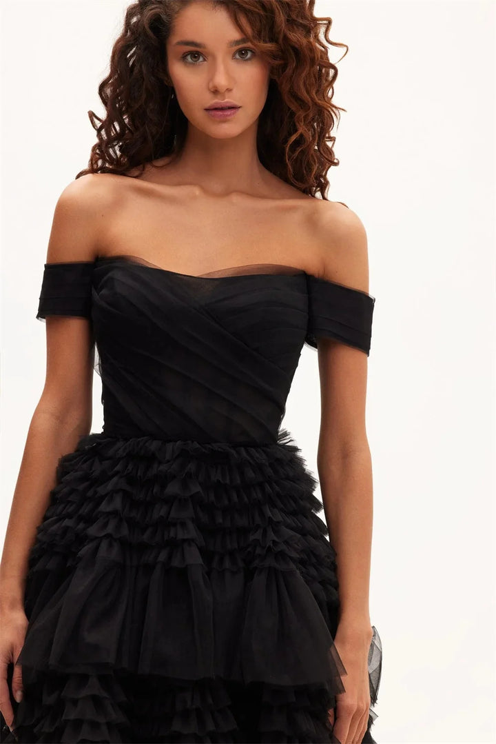 A model wearing an off-the-shoulder black maxi dress with a layered tulle ruffle and organza fabric.