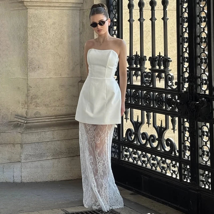 Woman wearing a white strapless top and sheer white skirt in front of an ornate black gate.